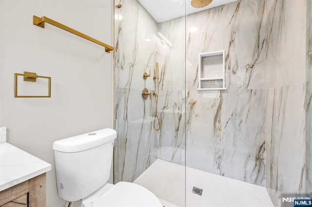 bathroom with toilet, a marble finish shower, and vanity
