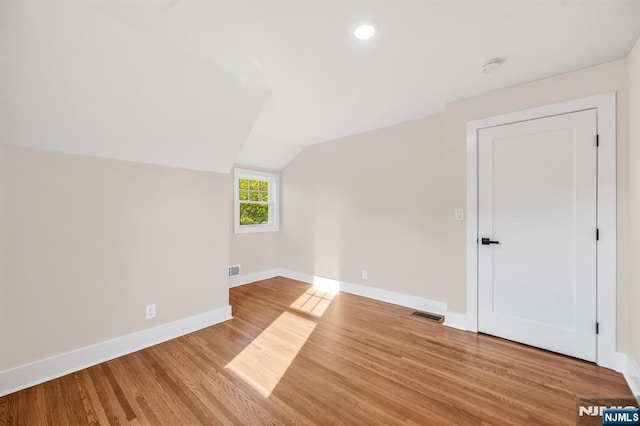 empty room featuring vaulted ceiling, baseboards, light wood-type flooring, recessed lighting, and a smoke detector