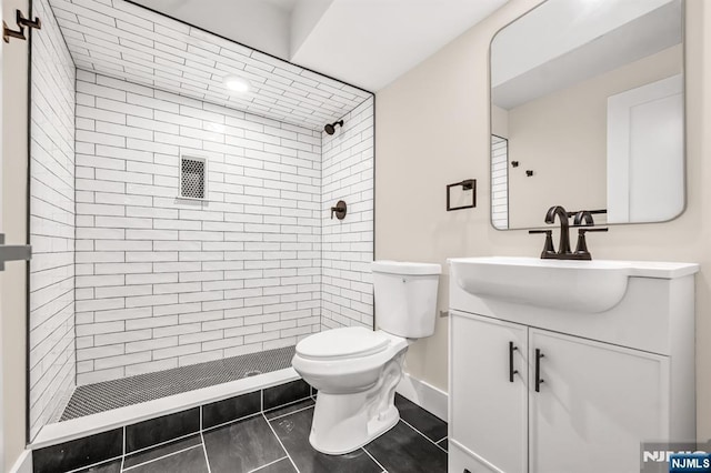 bathroom featuring toilet, a tile shower, vanity, tile patterned floors, and baseboards
