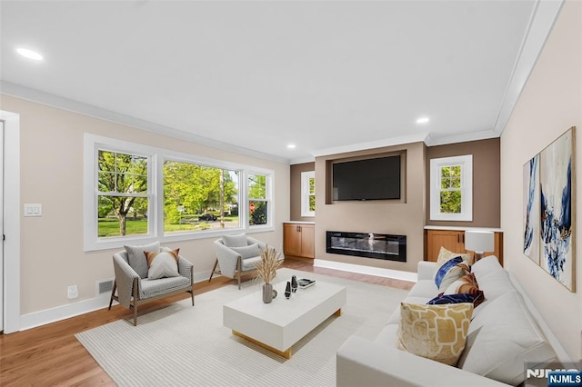living area with ornamental molding, light wood-style flooring, baseboards, recessed lighting, and a glass covered fireplace
