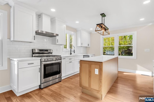 kitchen featuring stainless steel range with gas stovetop, wall chimney exhaust hood, light countertops, decorative backsplash, and a kitchen island