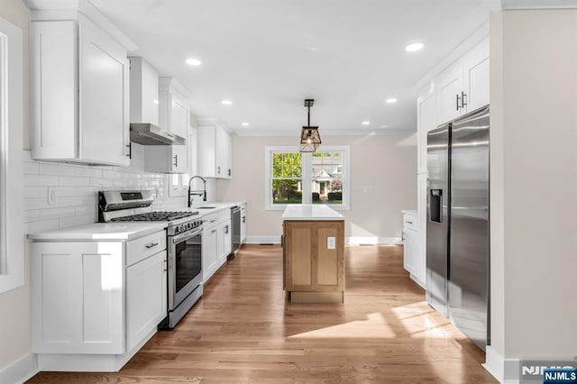 kitchen featuring appliances with stainless steel finishes, wall chimney range hood, a kitchen island, light countertops, and baseboards