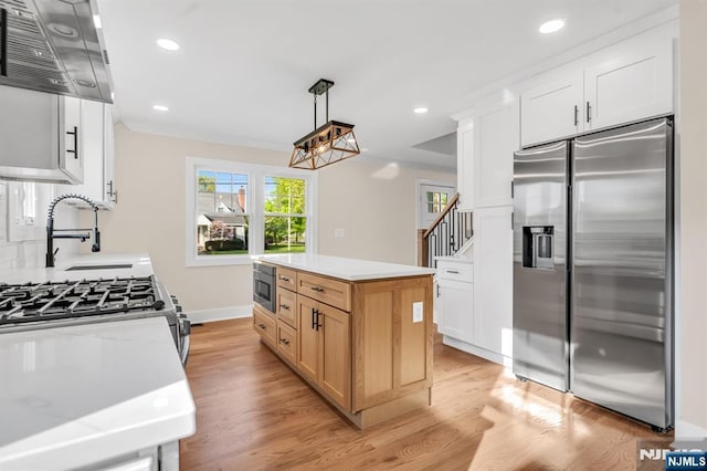 kitchen with appliances with stainless steel finishes, a sink, range hood, light wood-style floors, and recessed lighting