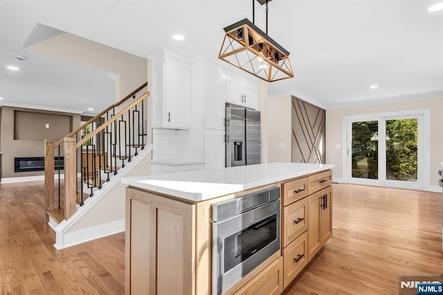 kitchen with stainless steel appliances, light wood-style flooring, a kitchen island, crown molding, and light countertops