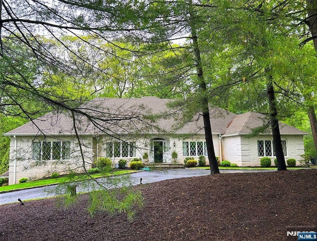 ranch-style home with curved driveway and a shingled roof
