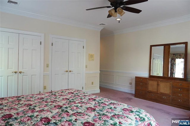 bedroom featuring carpet flooring, two closets, ornamental molding, a wainscoted wall, and ceiling fan