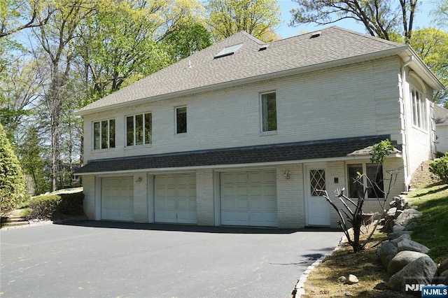 view of front of home featuring an attached garage, brick siding, driveway, and roof with shingles