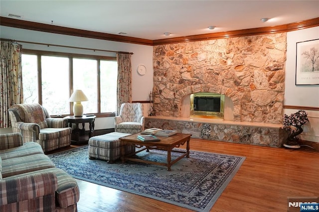living area featuring crown molding, wood finished floors, a stone fireplace, and baseboards
