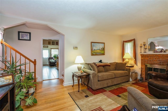 living room featuring stairs, light wood finished floors, a brick fireplace, and baseboards