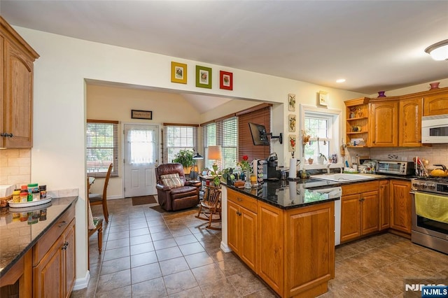 kitchen featuring gas stove, white microwave, a sink, brown cabinetry, and decorative backsplash