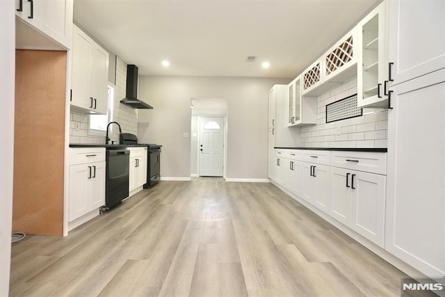 kitchen featuring wall chimney exhaust hood, dark countertops, black appliances, tasteful backsplash, and light wood finished floors