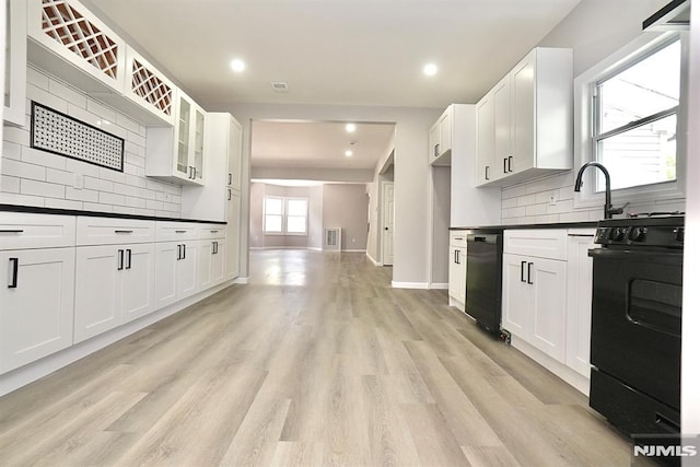 kitchen with black appliances, dark countertops, backsplash, light wood-style flooring, and glass insert cabinets