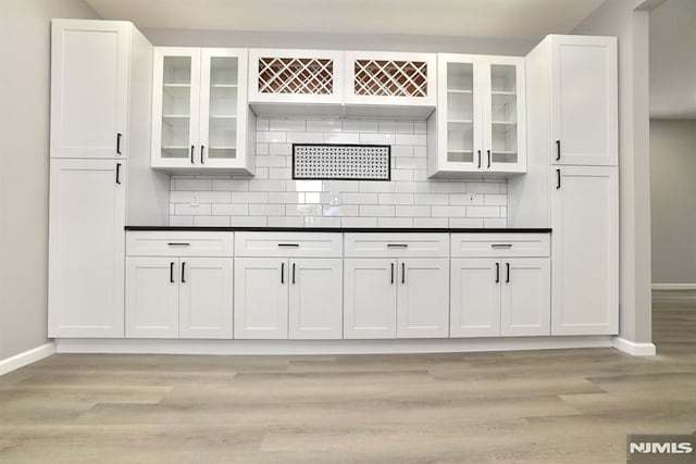 kitchen featuring baseboards, white cabinets, dark countertops, decorative backsplash, and light wood-style floors
