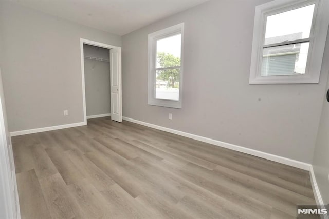 unfurnished bedroom featuring baseboards, wood finished floors, and a closet