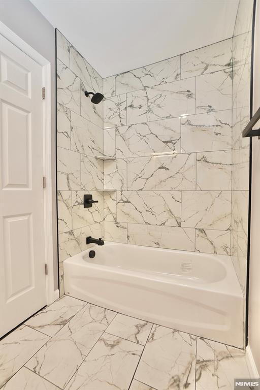 full bath featuring tub / shower combination and marble look tiles