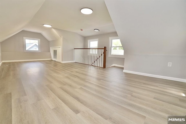 additional living space with vaulted ceiling, plenty of natural light, light wood-style floors, and baseboards