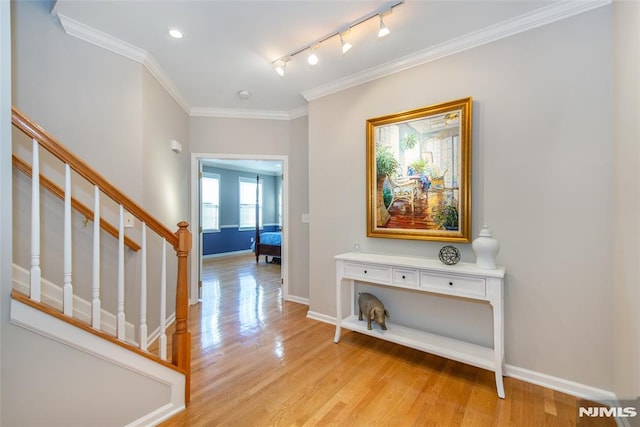 corridor featuring light wood-style flooring, baseboards, stairs, ornamental molding, and track lighting