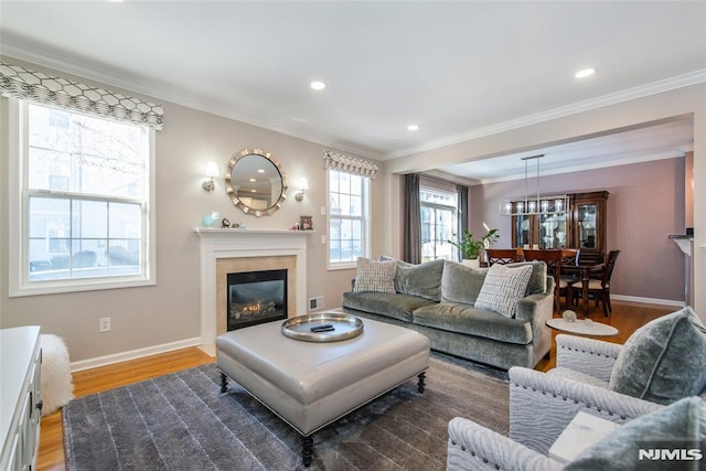 living area featuring light wood finished floors, a glass covered fireplace, baseboards, ornamental molding, and recessed lighting