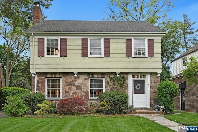 colonial-style house with stone siding, a chimney, and a front yard