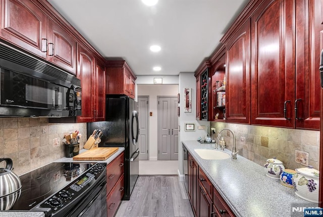 kitchen featuring reddish brown cabinets, black appliances, a sink, light wood-style floors, and backsplash