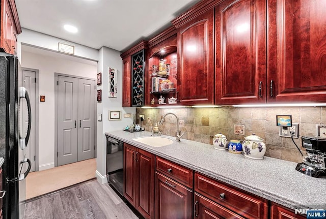 kitchen with reddish brown cabinets, a sink, black appliances, and light wood-style flooring