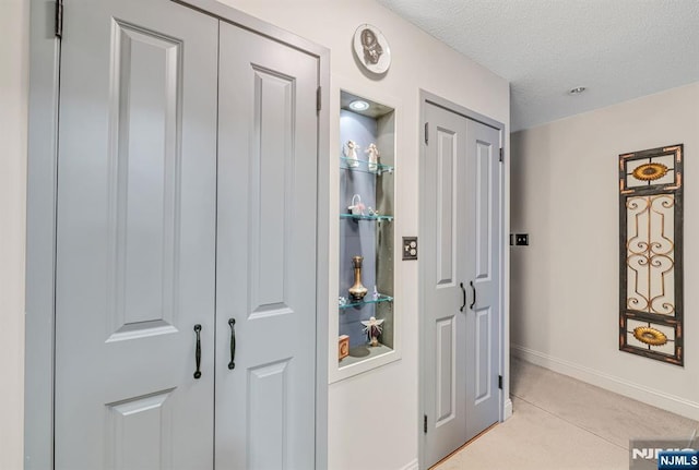 corridor with baseboards, a textured ceiling, and light carpet