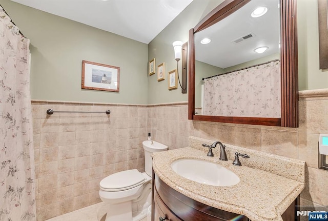 full bath with tile walls, vanity, toilet, and a wainscoted wall