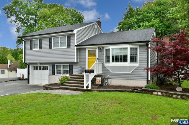 tri-level home featuring driveway, an attached garage, a chimney, a front lawn, and a shingled roof