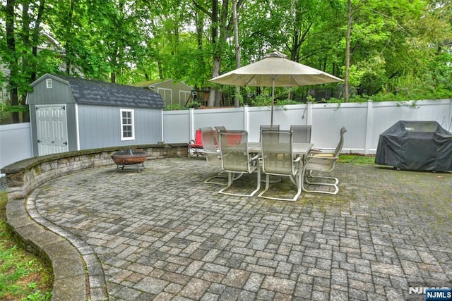 view of patio featuring an outdoor fire pit, a shed, a fenced backyard, grilling area, and outdoor dining area