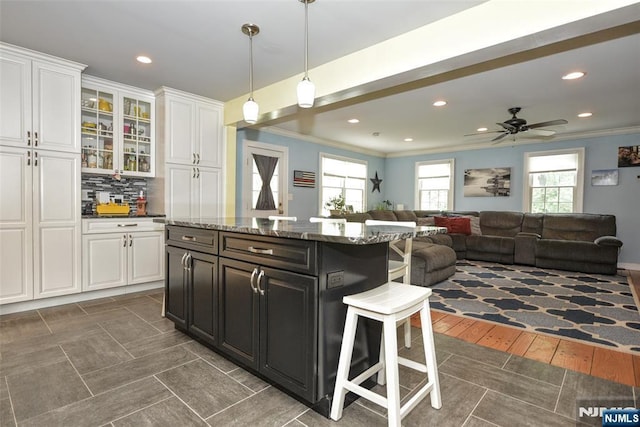 kitchen with a breakfast bar area, ornamental molding, white cabinetry, a kitchen island, and plenty of natural light