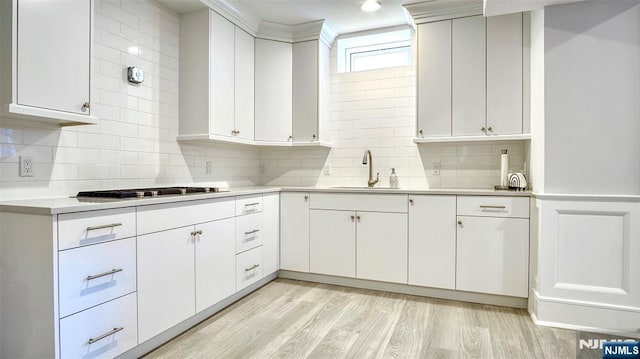 kitchen with a sink, light countertops, tasteful backsplash, and light wood finished floors
