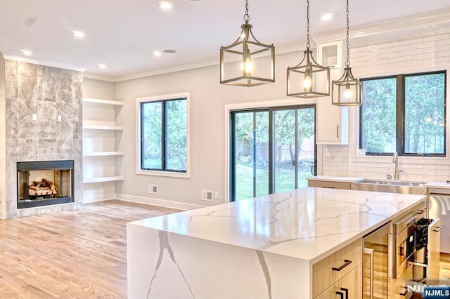 kitchen featuring a sink, light wood-style flooring, beverage cooler, light stone countertops, and crown molding