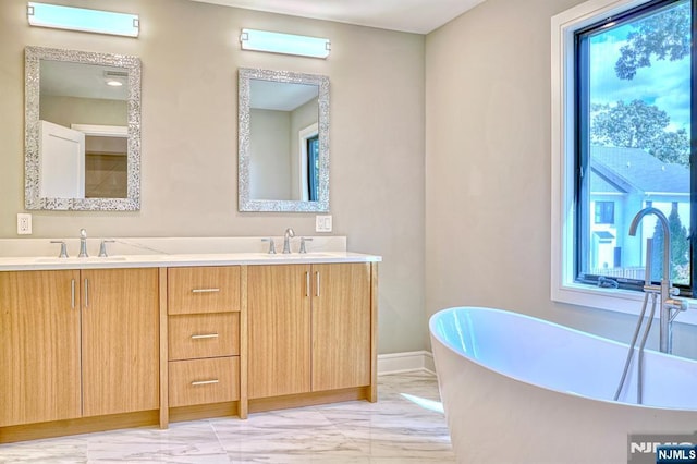 bathroom featuring marble finish flooring, double vanity, a freestanding bath, and baseboards