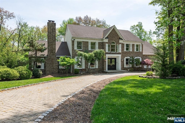 colonial-style house featuring a chimney, a front lawn, curved driveway, and french doors