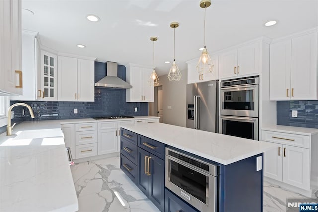kitchen featuring wall chimney exhaust hood, appliances with stainless steel finishes, blue cabinets, light marble finish flooring, and recessed lighting