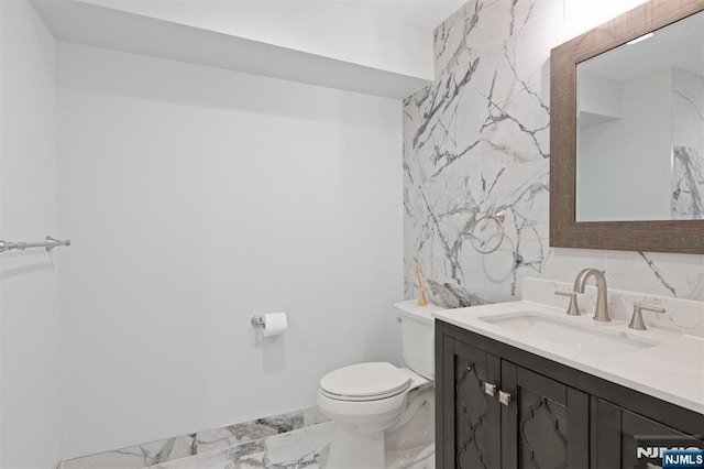 bathroom featuring marble finish flooring, toilet, vanity, and tile walls