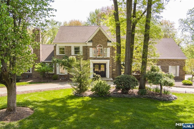 colonial home with a front lawn, brick siding, french doors, a chimney, and driveway