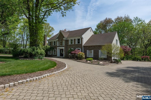 colonial house with curved driveway, brick siding, and a front lawn