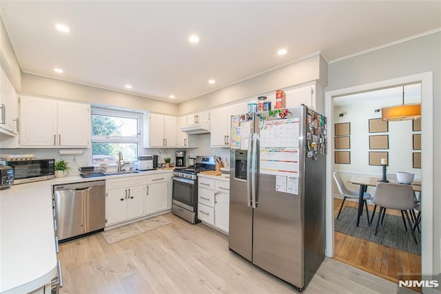kitchen with appliances with stainless steel finishes, a sink, under cabinet range hood, light wood-type flooring, and white cabinetry