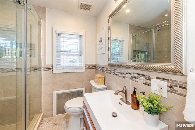 full bath featuring a stall shower, tile walls, toilet, vanity, and a wainscoted wall