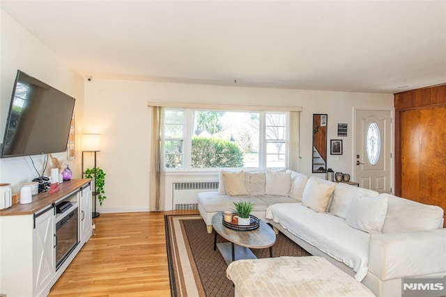 living area featuring radiator, light wood-type flooring, baseboards, and stairway