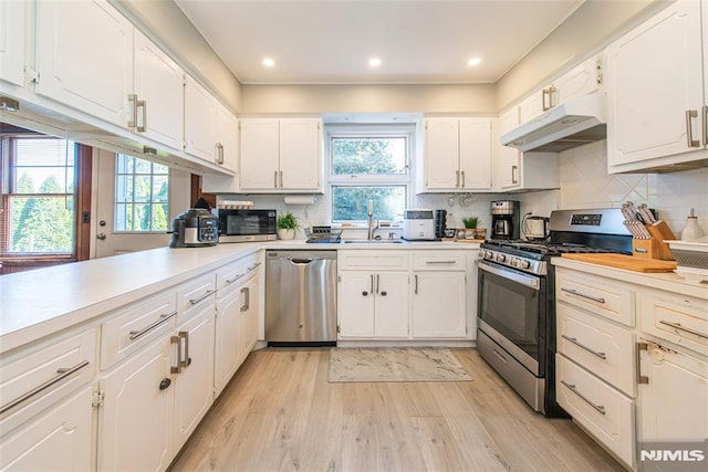 kitchen featuring appliances with stainless steel finishes, under cabinet range hood, light wood-type flooring, white cabinets, and recessed lighting