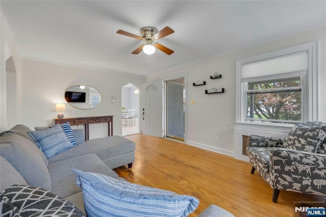 living area with arched walkways, crown molding, ceiling fan, wood finished floors, and baseboards