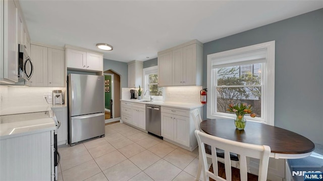 kitchen featuring appliances with stainless steel finishes, tasteful backsplash, light countertops, light tile patterned flooring, and a sink