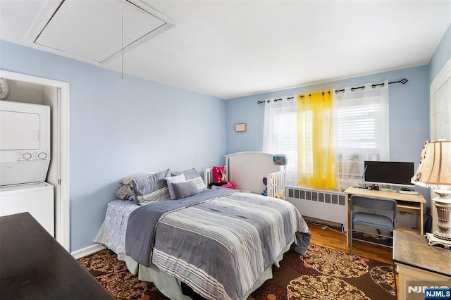 bedroom with stacked washer and clothes dryer, attic access, radiator heating unit, and wood finished floors