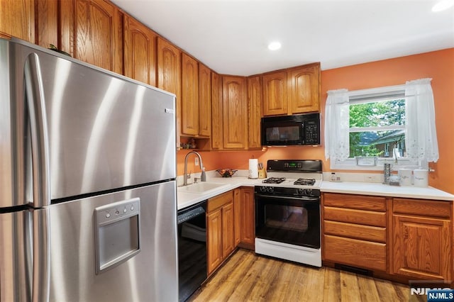 kitchen featuring black appliances, a sink, light wood finished floors, brown cabinets, and recessed lighting