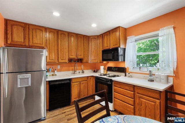 kitchen with black appliances, a sink, brown cabinetry, light countertops, and light wood finished floors
