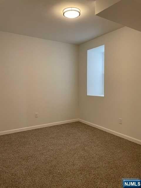 unfurnished room featuring baseboards and dark carpet