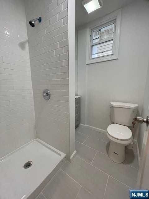 bathroom with tile patterned flooring, toilet, a stall shower, and baseboards