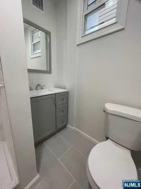 half bath with toilet, baseboards, vanity, and tile patterned flooring